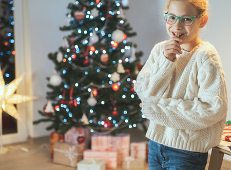 Cute happy teen girl with glasses eating christmas cookies with new years tree on background at homeの写真素材