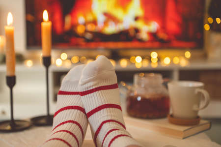 Close up cozy photo of feet in striped socks on side table with candles, teapot and cup  bevor fireplaceの写真素材