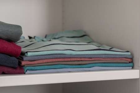 Closeup photo of neatly folded colorful clothes on shelf in wardrobeの写真素材