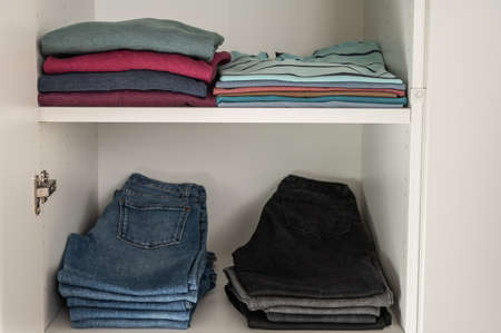 Neatly folded sweaters and jeans and other clothes on shelves in wardrobeの写真素材
