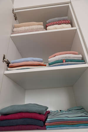 Pastel clothes neatly folded on shelves in wardrobeの写真素材