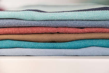Closeup photo of neatly folded colorful clothes on shelf in wardrobeの写真素材