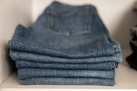 Closeup photo of pile of neatly folded blue jeans on shelf in wardrobeの写真素材