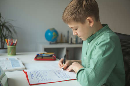 Diligent tenn student sitting at table and studying at home during online courseの写真素材
