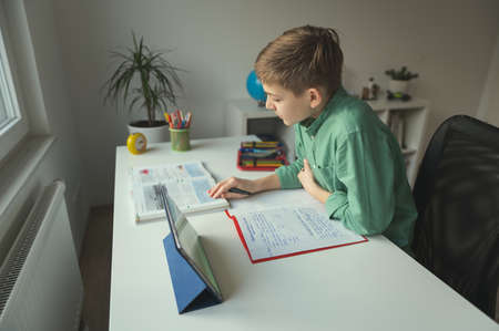 Diligent tenn student sitting at table and studying at home during online courseの写真素材