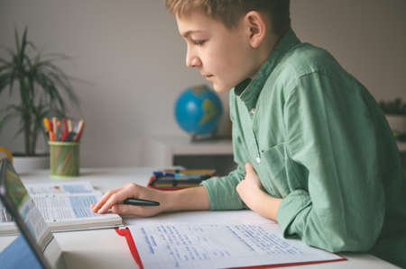 Diligent tenn student sitting at table and studying at home during online courseの写真素材