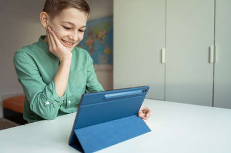Happy teen schoolboy have fun during online meeting or video call using tablet at homeの写真素材