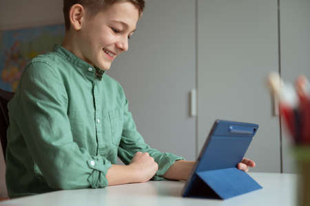 Happy teen schoolboy have fun during online meeting or video call using tablet at homeの写真素材