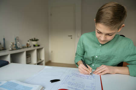 Diligent tenn student sitting at table and studying at home during online courseの写真素材
