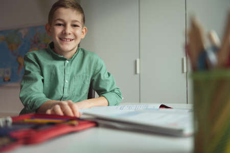 Portrait of cute teen schoolboy sitting at table at making homework at homeの写真素材
