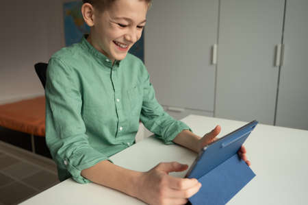 Happy teen schoolboy have fun during online meeting or video call using tablet at homeの写真素材