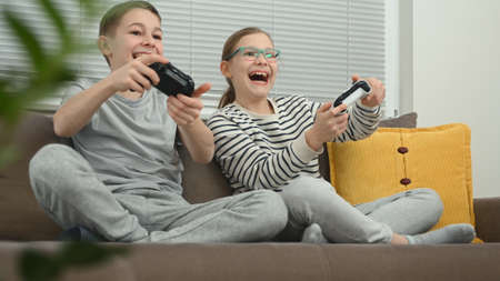 Excited brother and sister playing video game on a couchの写真素材