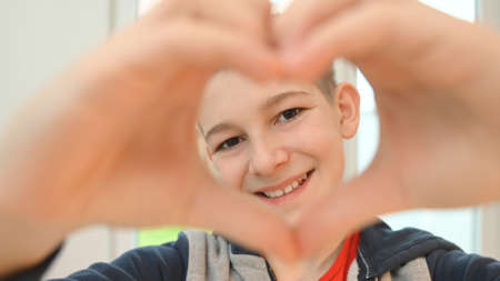 Smiling teen boy showing heart shape with his fingersの写真素材