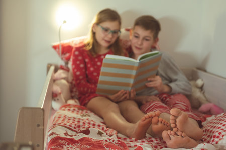 Teen brother and sister reading book in bed before night sleepの写真素材