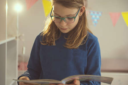 Teen girl in glasses reading text in notebook at homeの写真素材