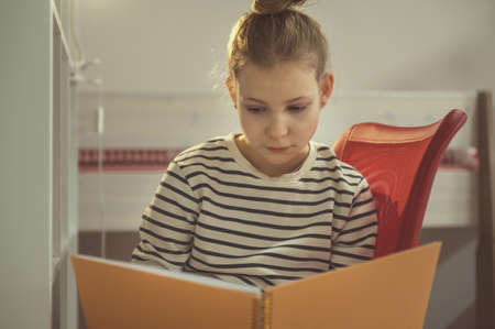 Teen blonde girl reading text in notebook at home
