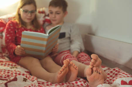 Teen brother and sister reading book in bed before night sleepの写真素材