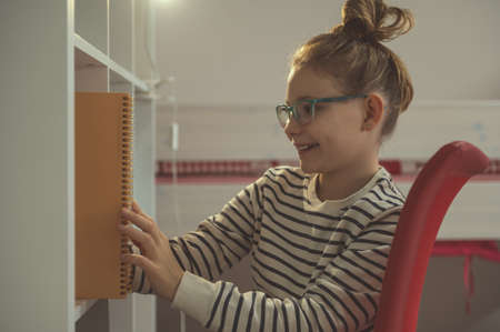 Teen girl in glasses reading text in notebook at home