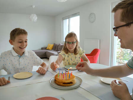 Portrait of happy children at birthday party with torte and colorful candles at table at homeの写真素材