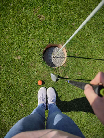 Photo from above of womans legs on green grass with golf ball and golf cue before  holeの写真素材