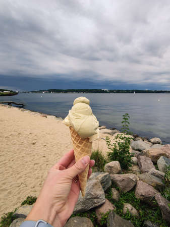 Woman's hand holding sweet tasty ice cream in waffle cone with sea on backgroundの写真素材