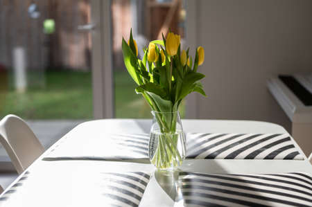 Beautiful glass vase with sresh yellow flowers on table in spring sunlightsの写真素材