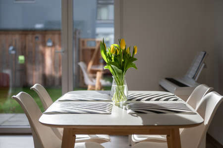 Beautiful spring photo of cozy home with yellow flowers on table and bright sunlightの写真素材