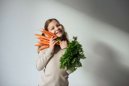 Smiling teen girl holding a bunch of fresh orange carrots with green leavesの写真素材