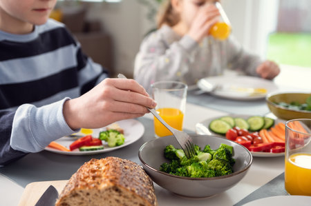 Children having breakfast: drinking orange juice and nailing fresh green broccoli on a forkの写真素材