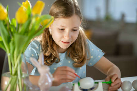 Cute little girl painting easter eggs at homeの写真素材
