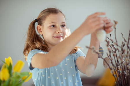 Happy teenage girl hangs easter eggs on tree branches at homeの写真素材