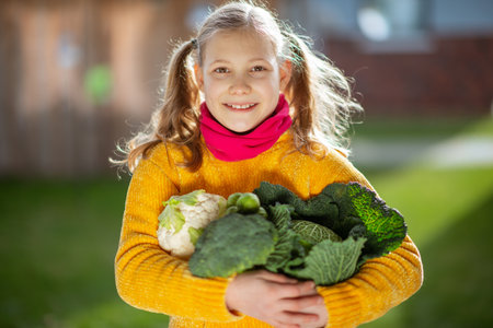 Funny little girl with two pigtails in yellow smiling with fresh autumn harvest in sunny rural gardenの写真素材