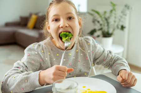 Cute teen girl eating green fresh broccoli during her lunchの写真素材