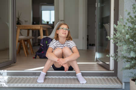Tired pretty school girl sitting on stair at home terrase an waiting for school holidaysの写真素材