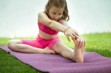 Happy beautiful child girl doing stretching exercises on yoga mat in sport uniform at home backyardの写真素材