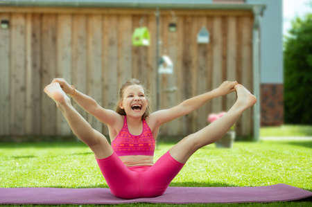 Happy sporty teenage girl practicing pilates on yoga mat on grass at backyardの写真素材