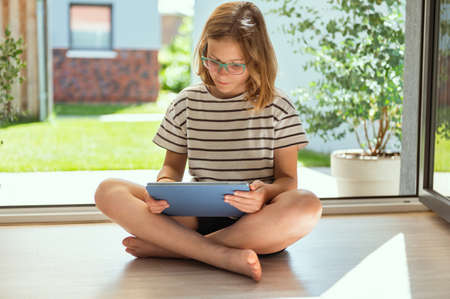 Pretty girl sitting with tablet and playing or surfing at summer sunny dayの写真素材