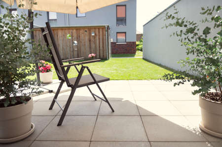 Cozy terrace with chairs under sun umbrella and big green plants in summer sunny dayの写真素材