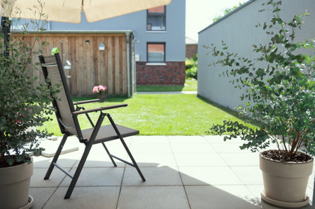 Cozy terrace with chairs under sun umbrella and big green plants in summer sunny dayの写真素材