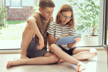 Teenage siblings children reading using tablet at home in summer sunny day