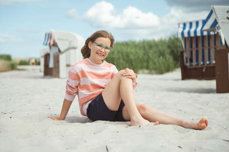 Happy pretty teen girl sitting on sunny white beach of Baltic sea at summer holidaysの写真素材