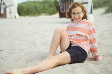 Happy pretty teen girl sitting on sunny white beach of Baltic sea at summer holidaysの写真素材