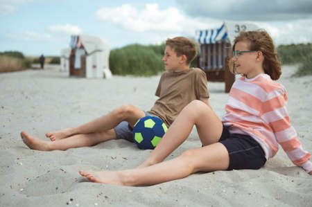 Cute teenage paar of children sitting on summer white beach at summer holidaysの写真素材