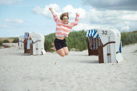 Pretty and happy teen girl joyful jumping on white beach at Baltic sea at summer holidaysの写真素材