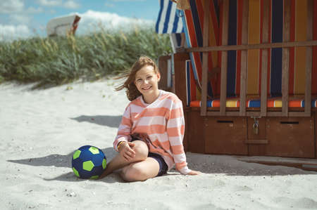 Cute little girl sitting on white sand with beach ball on beautiful beach with dunes on Baltic seaの写真素材