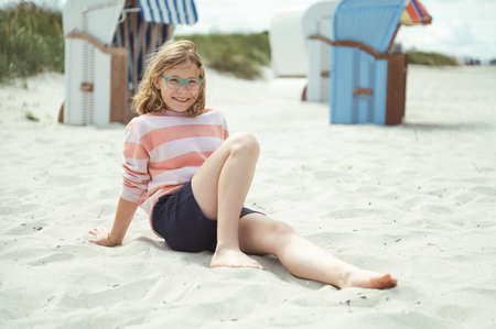 Happy pretty teen girl sitting on sunny white beach of Baltic sea at summer holidaysの写真素材