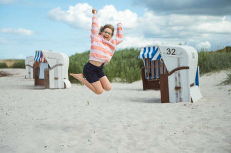 Pretty and happy teen girl joyful jumping on white beach at Baltic sea at summer holidaysの写真素材