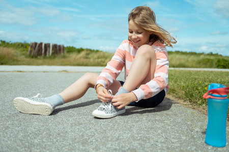 Pretty teen girl smiling and sitting on ground and tie her shoelaces at summer dayの写真素材
