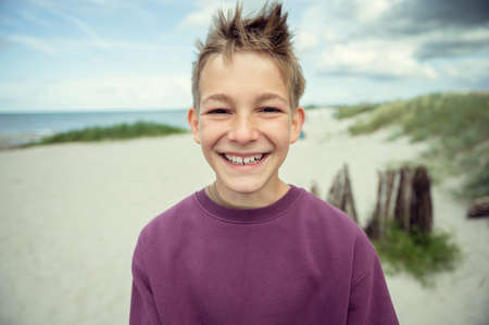 Portrait of handsome teenage boy on beach with white sand at windy summer dayの写真素材