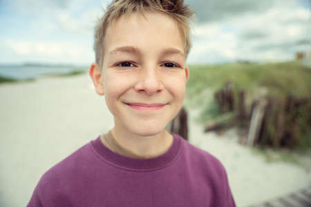 Portrait of handsome teenage boy on beach with white sand at windy summer dayの写真素材